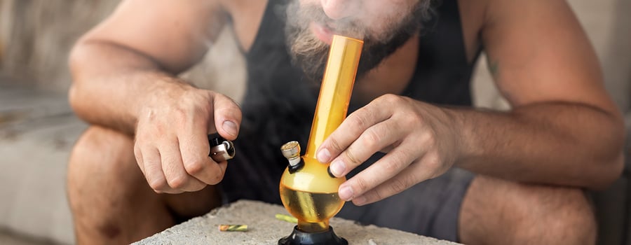 Persona fumando hachís de un bong de vidrio, exhalando humo espeso.